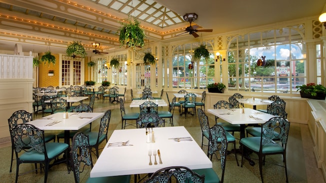 The charming interior of Tony’s Town Square Restaurant at Magic Kingdom park, with tables and chairs, ceiling fans and hanging plants