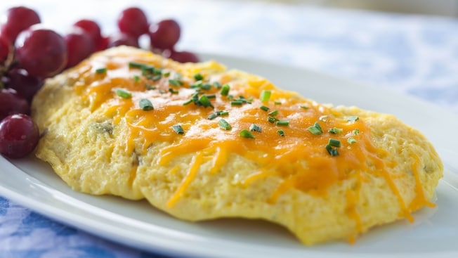 An omelet topped with melted cheddar and chives, accompanied by red grapes