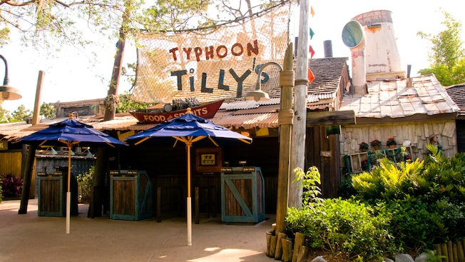 Entrance to a quick service restaurant, with 2 patio umbrellas and a sign on netting that reads ‘Typhoon Tilly’s, Food and Spirits’