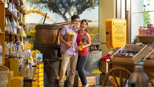 A man holds an Immortelle flower between his teeth adjacent to a woman carrying a sack of dried lavender inside L’Occitane