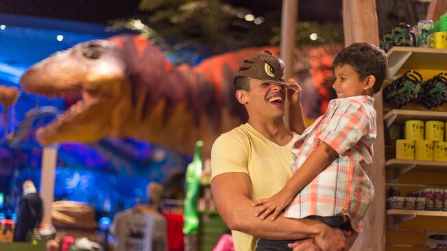 Un niño coloca una gorra de dinosaurio en la cabeza de su padre