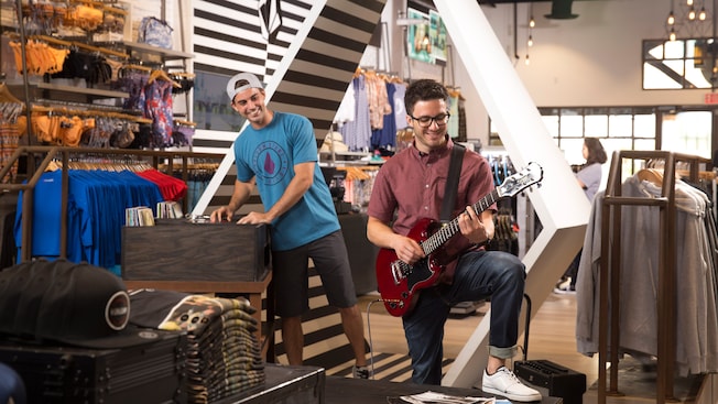 A young man plays a display guitar while his male friend looks on with amusement inside Volcom