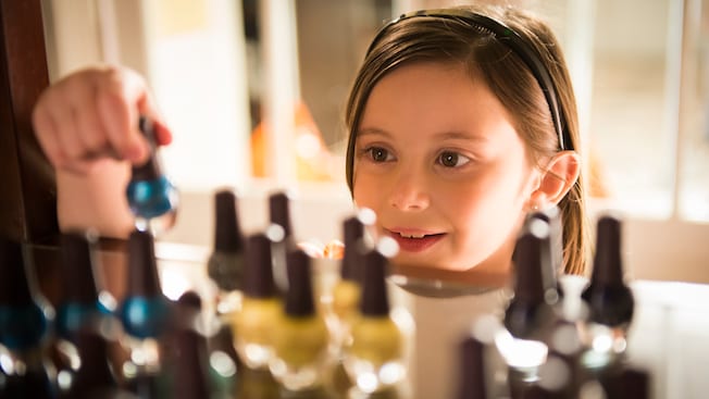 A girl chooses a bottle of nail polish on a shelf that holds several bottles of polish