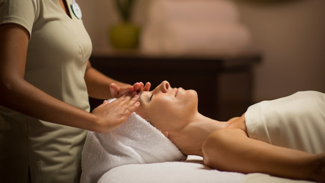 A masseuse gently rubs the forehead of a woman lying on a massage table