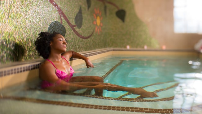 A woman in a bathing suit sits in an indoor spa pool and relaxes