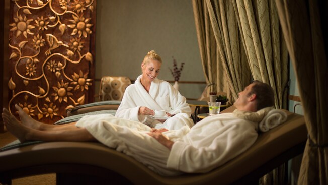 A husband and wife, wearing matching robes, relax on reclining chairs