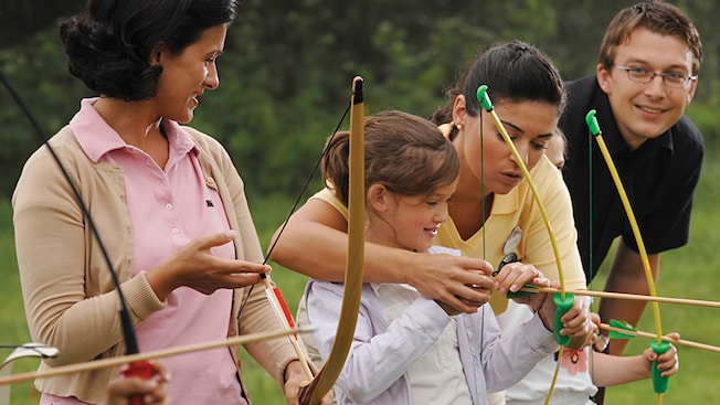 A young female Guest receiving firsthand instructions from a Cast Member during an archery lesson