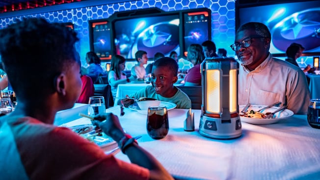 A man and 2 young boys smile at each other while dining inside Worlds of Marvel restaurant A man and 2 young boys smile at each other while dining inside Worlds of Marvel restaurant