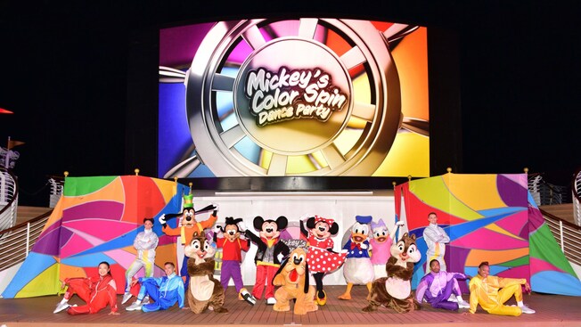 A scene from Mickey’s Color Spin Dance Party featuring Disney Characters and Cast Members posing for a picture on the Funnel Vision Deck Stage of a Disney Cruise Line ship