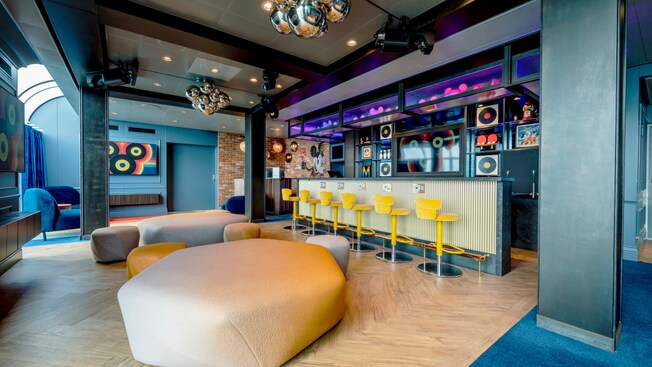 El club para jóvenes The Hideaway en el Disney Treasure con televisores, sofás, pufs grandes y un bar con asientos