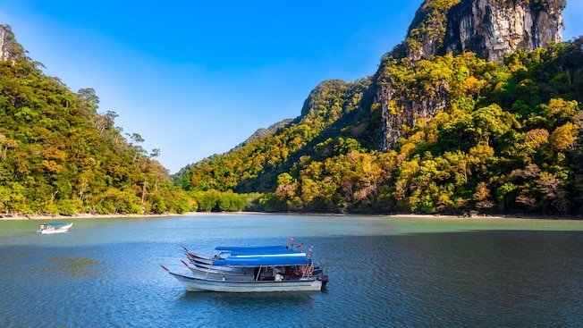 A tour boat cruising past dramatic limestone cliffs and mangrove forests in Langkawi, Malaysia A tour boat cruising past dramatic limestone cliffs and mangrove forests in Langkawi, Malaysia