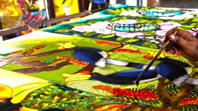 An artisan painting a vibrant batik canvas depicting butterflies, hornbills and tropical foliage