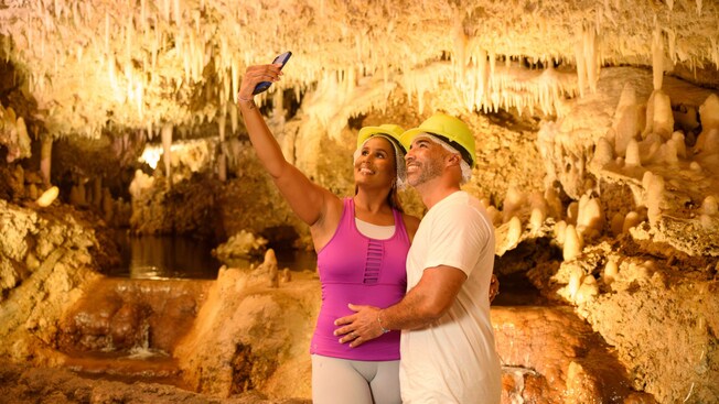 A couple taking a selfie in a cave filled with stalactites, stalagmites and a pool of water