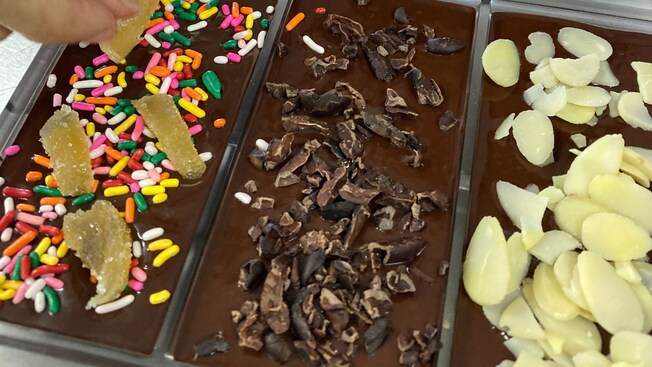 A hand adding various toppings to chocolate bars in a molding tray
