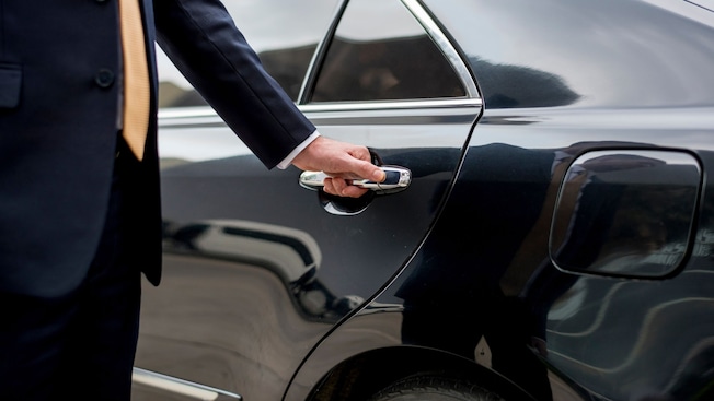 A professional driver in a suit opening the rear door of a luxury sedan A professional driver in a suit opening the rear door of a luxury sedan