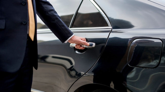 A professional driver in a suit opening the rear door of a luxury sedan A professional driver in a suit opening the rear door of a luxury sedan
