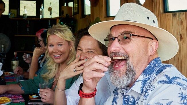 A man eating a marinated baked cricket with others watching closely