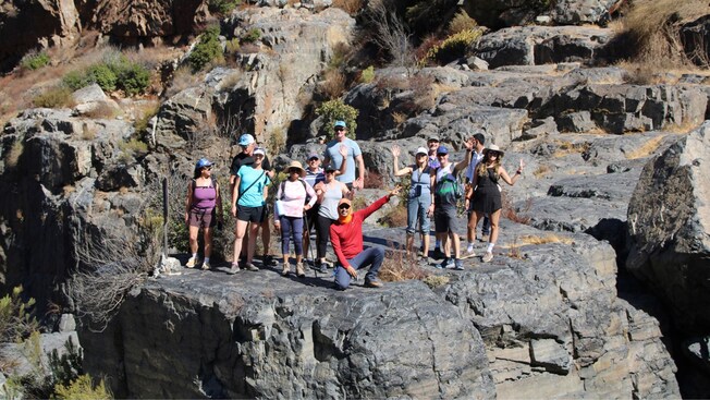 A group of Guests posing with a guide on top of a cliff at El Salto Canyon
