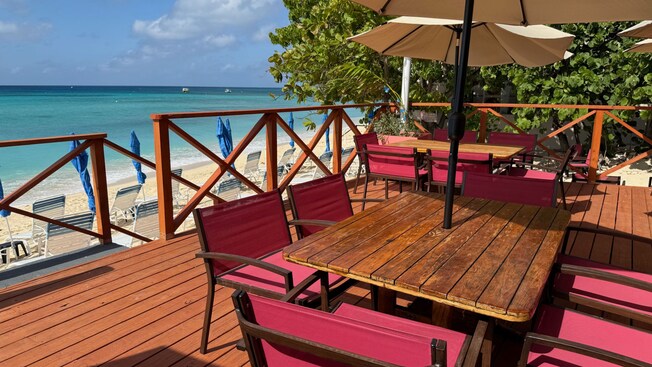 Two tables with chairs and umbrellas on a beachfront deck