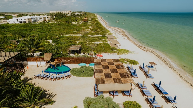 A pool and many lounge chairs, some under a checkered canopy, on a beach fronting the calm waters of the Gulf of Mexico A pool and many lounge chairs, some under a checkered canopy, on a beach fronting the calm waters of the Gulf of Mexico