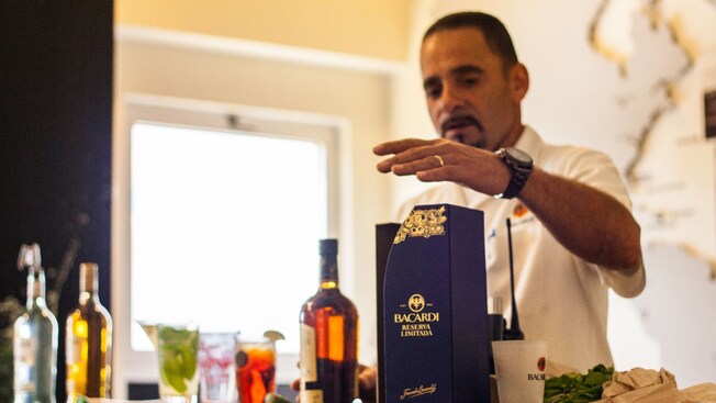 A Casa Bacardi tour guide giving an explanation on drink preparation behind a counter with rum bottles and drinks