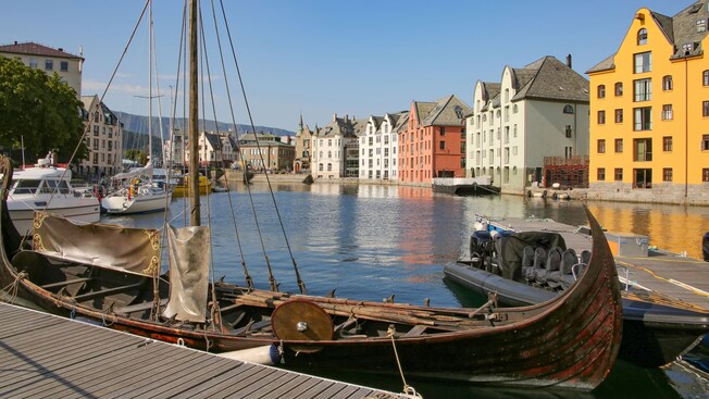 A Viking longship moored at the harbor with buildings lining the waterfront