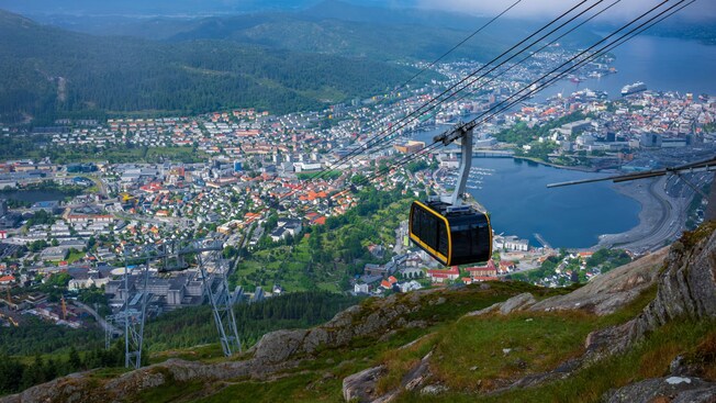 A cable car gondola descending over a coastal town surrounded by mountains