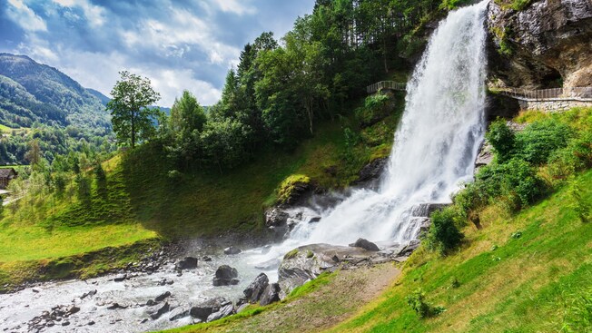 A large waterfall cascading down moss covered rocks surrounded by trees and mountains