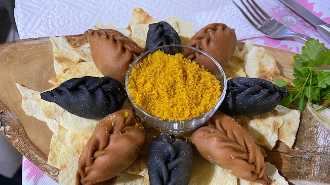 Culurgiones placed in a circle on top of pita chips with a bowl of yellow seasoning in the center Culurgiones placed in a circle on top of pita chips with a bowl of yellow seasoning in the center