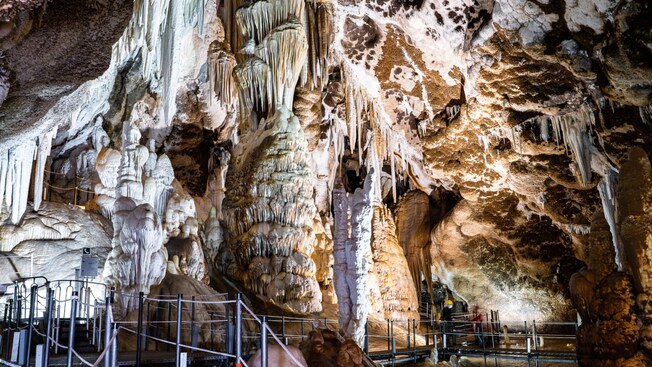 A large underground cave with towering rock formations surrounding metal walkways with railings