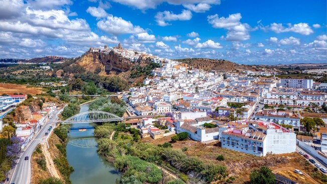Aerial view of a historic hillside town with buildings, a river and a bridge