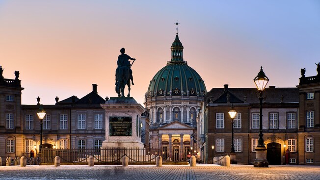 The exterior of Amalienborg Palace in Copenhagen, featuring an equestrian statue and the dome of Frederik's Church