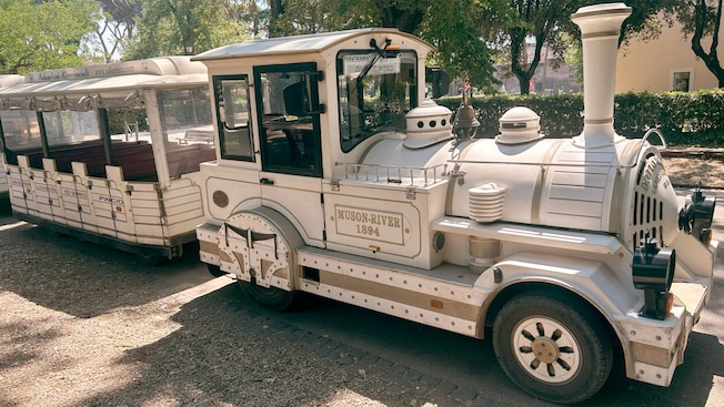 An empty trolly parked on a gravel path surrounded by trees and lush greenery An empty trolly parked on a gravel path surrounded by trees and lush greenery