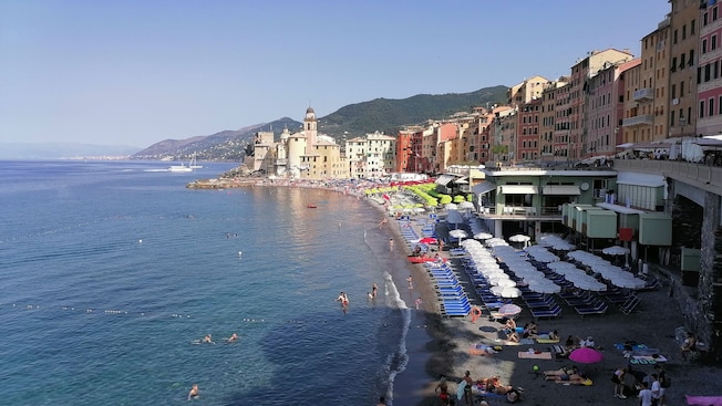 The shoreline of Camogli Beach with buildings, lounge chairs and umbrellas in Genoa, Italy The shoreline of Camogli Beach with buildings, lounge chairs and umbrellas in Genoa, Italy