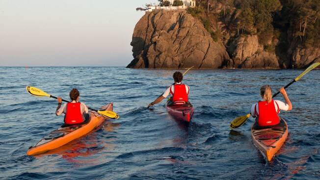 Three people kayaking on the water near a cliff in Portofino, Italy