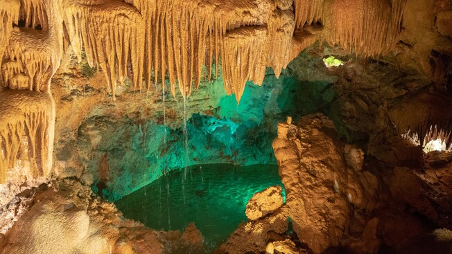 An underground cave with stalactites hanging from the ceiling and a pool surrounded by rock formations