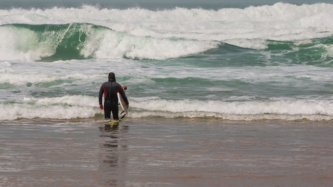 A surfer standing on a beach with his back turned and holding a surfboard A surfer standing on a beach with his back turned and holding a surfboard