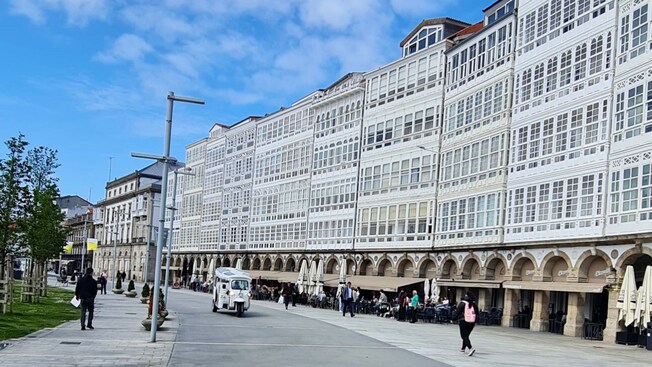 Una fila de edificios históricos con fachadas y columnas de vidrio, con gente caminando y un tuk tuk
