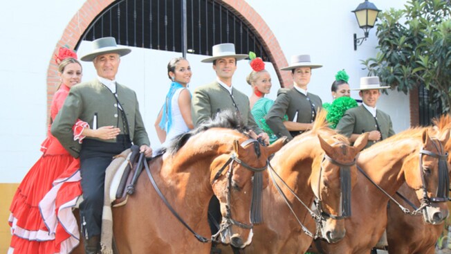 A row of 4 horses, each with a male and a female rider in flamenco costumes