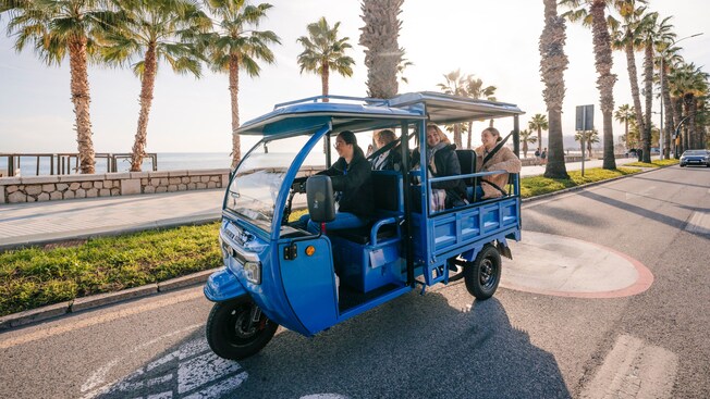 A group of Guests riding a Tuk Tuk along a palm tree lined road near the Málaga coastline