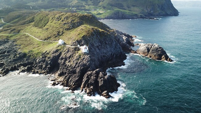 Two lighthouse buildings perched on a rocky cliff dropping into the ocean