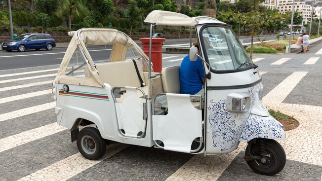A tuk tuk decorated with blue floral patterns parked on a cobblestone street