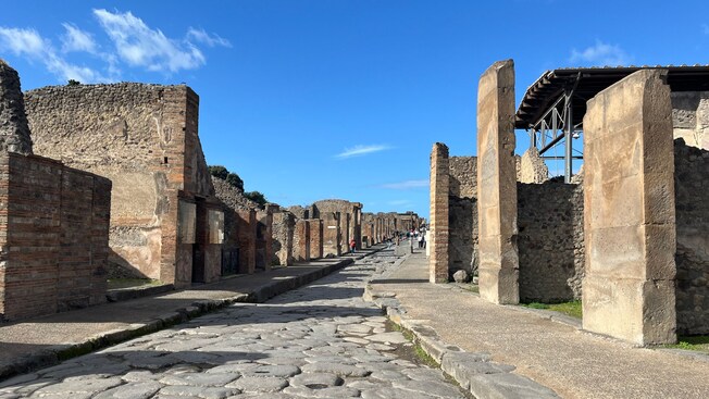 Ancient stone street lined with ruins of buildings in the archaeological site of Pompeii