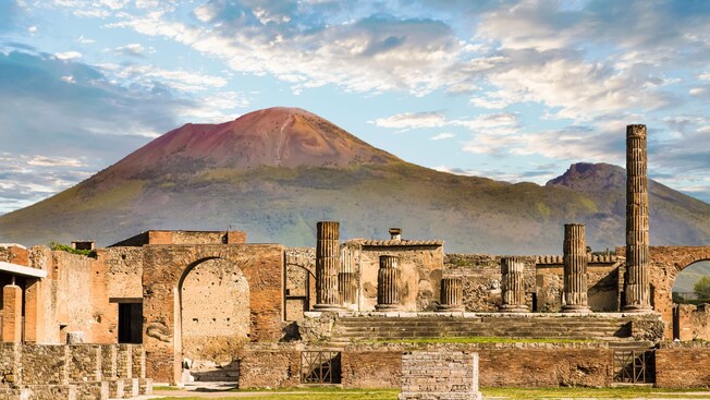 Ancient ruins of Pompeii with Mount Vesuvius in the background under a partly cloudy sky