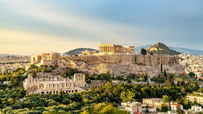 The Acropolis hilltop with the Parthenon temple surrounded by ancient ruins and vegetation The Acropolis hilltop with the Parthenon temple surrounded by ancient ruins and vegetation