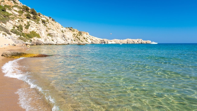 A sandy beach with clear water gently lapping the shore, surrounded by rocky cliffs A sandy beach with clear water gently lapping the shore, surrounded by rocky cliffs
