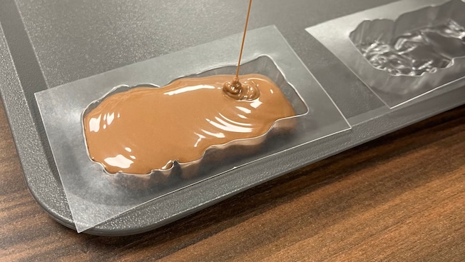 Melted milk chocolate being poured into a mold on a baking sheet Melted milk chocolate being poured into a mold on a baking sheet