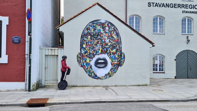 A Guest riding a Segway past a mural of a face on a Stavanger Port Authority building