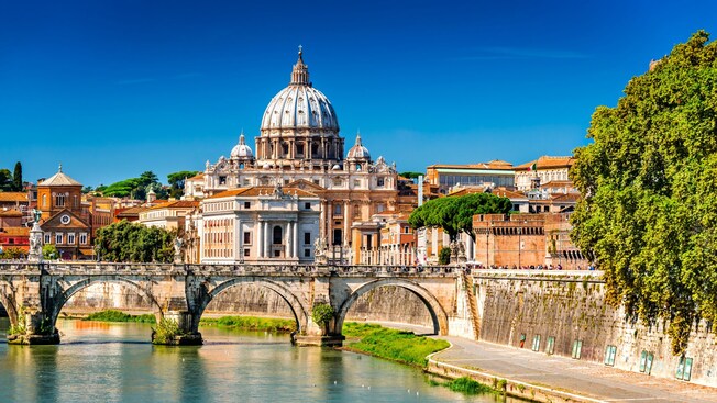 St. Peter’s Basilica in Vatican City seen beyond a historic bridge over the Tiber River in Rome