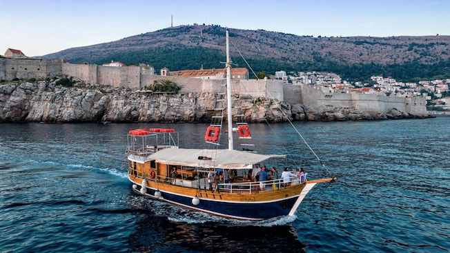 A wooden boat sails past the ramparts of a medieval city in Dubrovnik, Croatia A wooden boat sails past the ramparts of a medieval city in Dubrovnik, Croatia